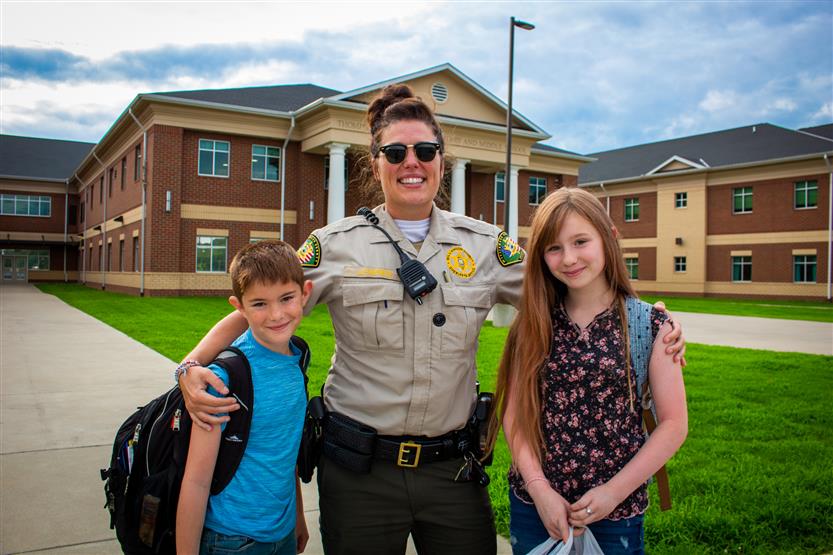 A School Resource Officer smiles while standing next to two students